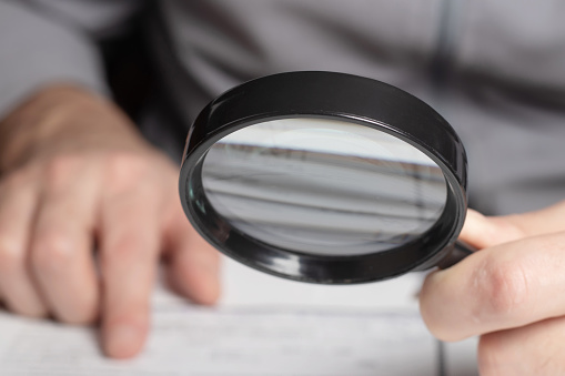 Man looking through a magnifying glass to documents.