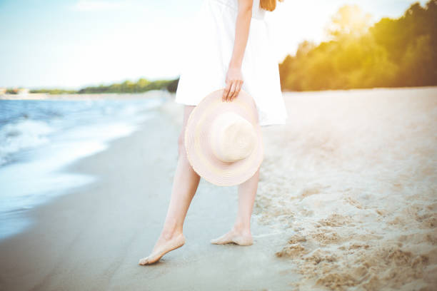 istock Young woman on a beach holding a white hat. Legs close up 1492374260
