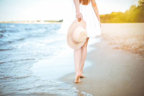 istock Young woman on a beach holding a white hat. Legs close up 1492374273