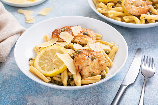 Chicken piccata pasta with lemon and capers in a white bowl