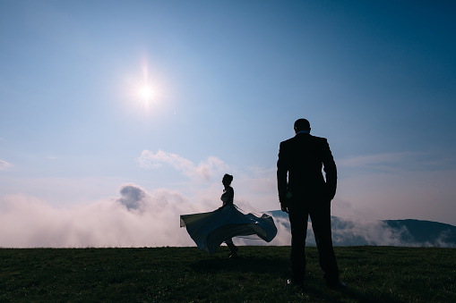 Beautiful silhouette of a newlywed couple in a field with a warm summer sunset against the background of the sky, the girl is spinning in a dress.