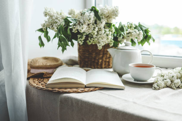 istock Open book, cup of tea and teapot, white lilac basket and hat, summer composition 1492377087