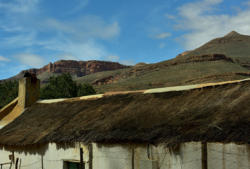An old original thatched roof house in the rural hamlet of Wupperthal with the rugged Cederberg mountains and cloudscape behind it.