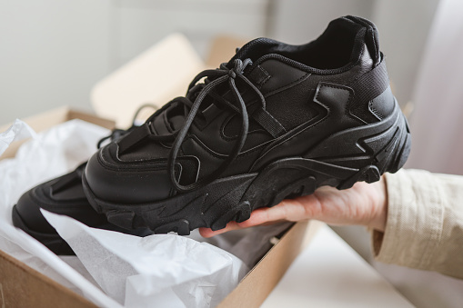 Unpacking women's shoes, stylish black sneakers in hands.