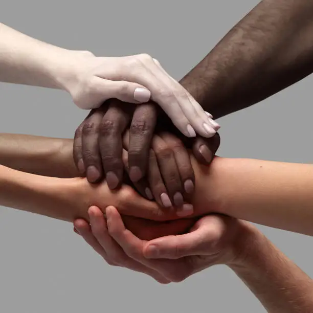Support and care. Human hands of different race, skin color holding together over grey background. Humanity. Acceptance. Concept of human relation, community, togetherness, symbolism, culture