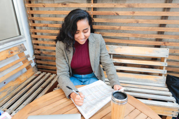 young latin woman looking for job in the newspaper, at a coffee shop. - job search newspaper coffee shop cafe imagens e fotografias de stock