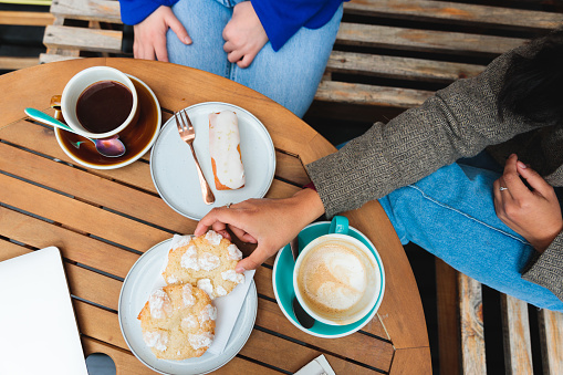 Coffee Delights: High angle view of  Young Unrecognizable Women drinking Coffee and eating Sweet Pastries in a Cozy Cafe Patio