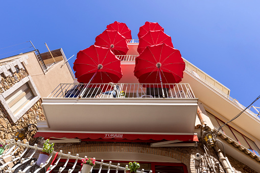 Castelmola, Sicily, Italy - April 28, 2023: View of the restaurant balconies with large red sun umbrellas against the blue sky