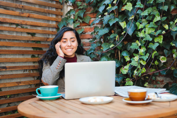 istock Young Latina Businesswoman, dressed in a blazer, Working Remotely from a Cozy Cafe with Laptop and Phone 1492380708