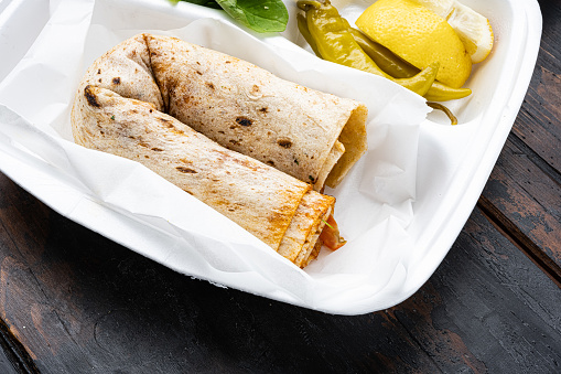Turkish Style chicken roll Tavuk Durum tantuni, in plastic pack container delivery lunch box, on old dark  wooden table background