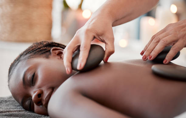 black woman, hot stone massage, spa and hands of masseuse, holistic and wellness, therapy and treatment. health, peace of mind and rocks with zen, stress relief for people and back skin detox - lastone therapy imagens e fotografias de stock