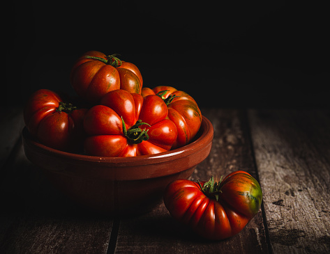 still life of beef heart tomatoes, organic in an earthenware dish on a wooden table, with soft light in front, copy space