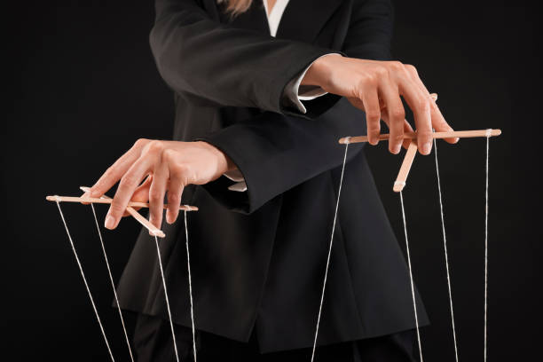 istock Woman in suit pulling strings of puppet on black background, closeup 1492387573