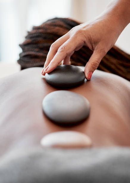 femme noire, mains et rock sur le dos dans le traitement de spa pour la relaxation, le soulagement du stress ou le massage au complexe. main de masseuse appliquant des pierres à une femme afro-américaine en physiothérapie pour le bien-être - lastone therapy spa treatment massaging massage therapist photos et images de collection