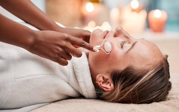 massage du visage, rouleau et femme au spa avec thérapeute, traitement et soins de la peau, soins personnels et quartz rose. thérapie holistique dans un complexe de luxe, peau saine et bien-être, mains et massage avec beauté - massaging spa treatment stone massage therapist photos et images de collection