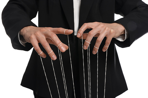 Woman in suit pulling strings of puppet on white background, closeup