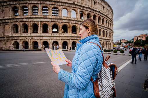 Young woman tourist using a map in front of the Colosseum in Rome, Italy