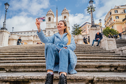 Young cheerful woman tourist taking a selfie in front of the famous Spanish steps in Rome, Italy