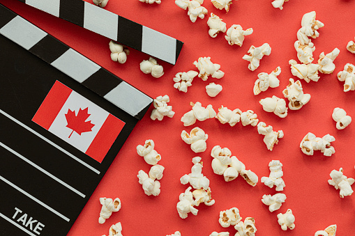 Movie clapper with Canadian flag and popcorn on red background. Representing film industry in Canada.
