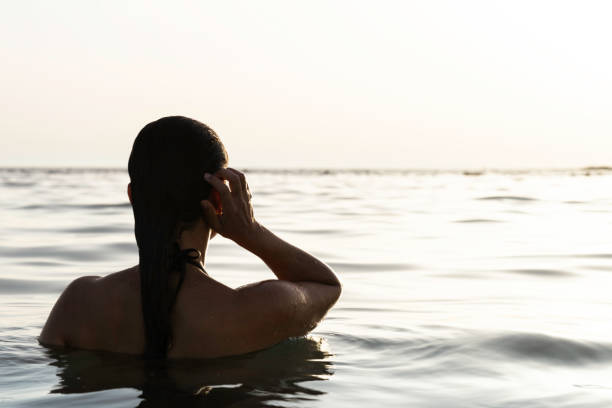 Backview of Woman in Sea Back view of caucasian woman with long hair in sea looking at the horizon. waist deep in water stock pictures, royalty-free photos & images