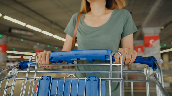 Closeup of young Asian female with shopping cart trolley and walking in car parking. Shopping in the supermarket concept.