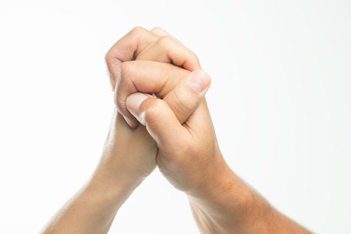 Two unrecognizable caucasian peoples hands are holding each other in front of gray background.