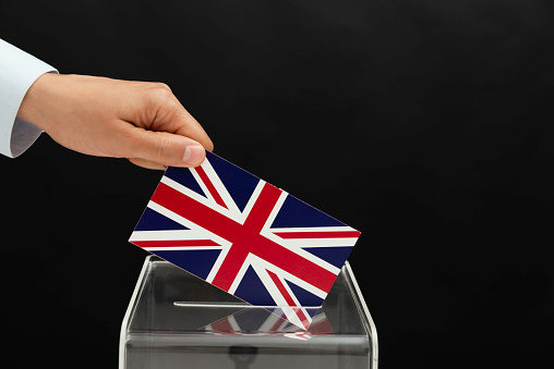 Human hand is inserting united kingdom flag into ballot box.