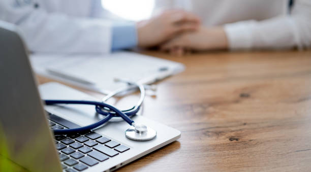 istock Stethoscope and laptop computer are lying on the wooden table while doctor's hands reassuring a patient at the background. Medicine concept 1492398902
