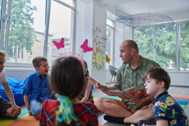 istock Reading time in an elementary school or kindergarten, a teacher reading a book to children in an elementary school or kindergarten. The concept of pre-school education. Selective focus 1492400612
