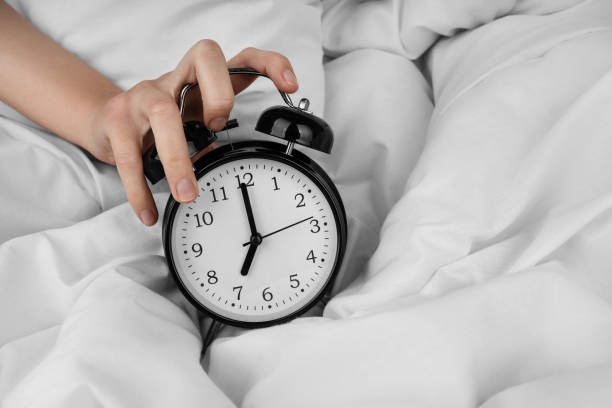 istock Woman's hand turning off black alarm clock on bed 1492400860