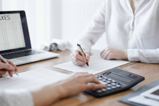istock Two accountants using a laptop computer and calculator while counting taxes at wooden desk in office. Teamwork in business audit and finance 1492401096