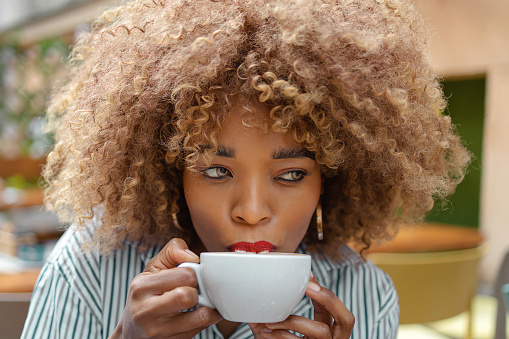 Closeup image of a black woman holding and drinking hot coffee in a street cafe