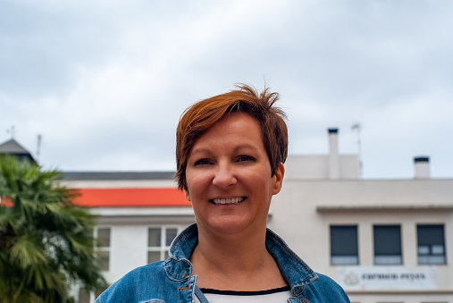 Middle-aged woman smiling in front of a building.