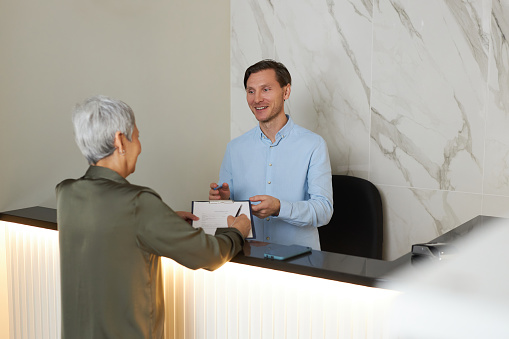 Portrait of smiling young man helping senior woman registering to visit doctor in clinic