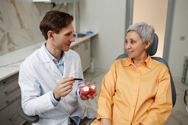 homme dentiste consultant une femme âgée en clinique dentaire et tenant un modèle de dent - dentist surgery dental hygiene using voice photos et images de collection