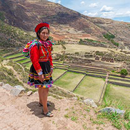 Peruvian quechua indigenous woman in traditional clothing and Tipon inca agriculture terraces, Cusco, Peru.