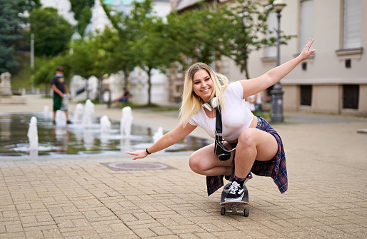 Happy teenager girl skateboarding on city streets while listening to music on headset - Keep smiling and enjoying life concept - Backlit summer lifestyle photo