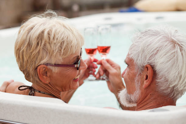 Brindis pareja Senior con champagne en una bañera de hidromasaje - foto de stock