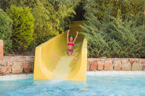 Multi-ethnic family with two children having fun at water park.  Focus on mother and daughter going down slide.