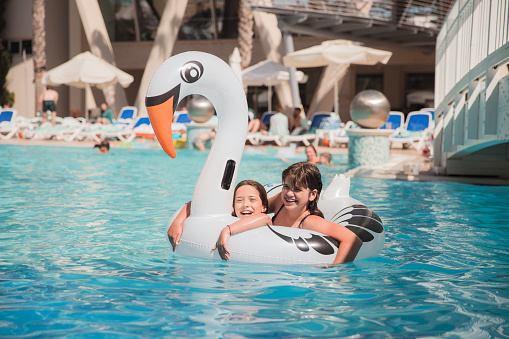 Happy young girls having fun at pool, floating on a big inflatable swim swan-shaped ring