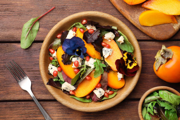 istock Delicious persimmon salad with cheese and pomegranate served on wooden table, flat lay 1492420945