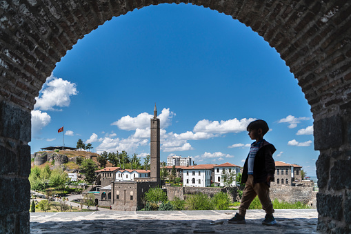 The view of the mosques and structures in the inner castle from the Diyarbakir walls. boy walks on the walls.  The photograph was taken from inside the architectural arch of the city walls. The buildings in the image are the administrative buildings of the palace. Shot with a full-frame camera in daylight.