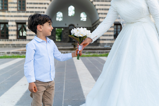 boy giving bridal flowers to bride. his shy face is shot in close-up while giving the flower. Shot with a full-frame camera in daylight.