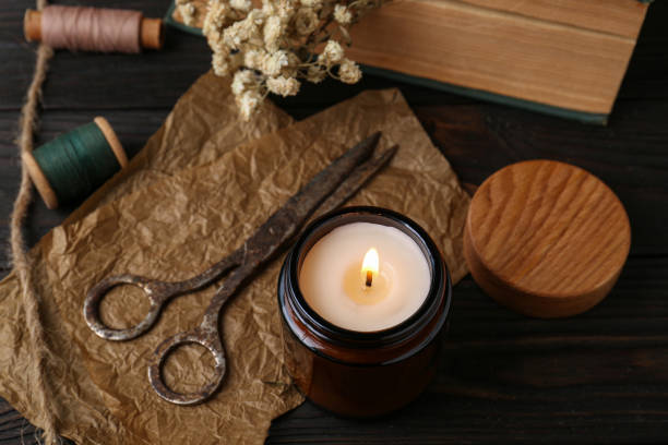 istock Burning scented candle, old scissors, book, threads and flowers on wooden table 1492422446
