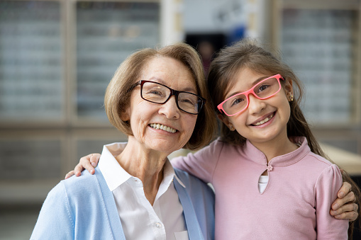 Portrait of a happy Latin American grandmother and granddaughter wearing glasses at the opticians store and smiling at the camera
