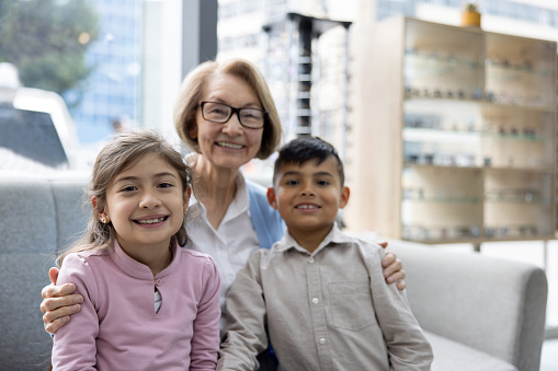 Happy Latin American grandmother smiling with her grandchildren at the optometry store while wearing her glasses