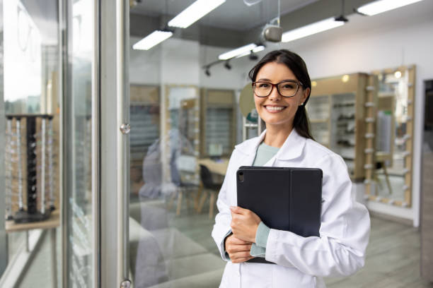 Happy optician working at an optometry store using a tablet Portrait of a happy Latin American optician working at an optometry store using a tablet computer and looking at the camera optometry stock pictures, royalty-free photos & images