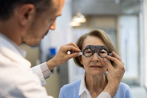 Senior Latin American woman getting an eye exam at the optician and looking through a phoropter