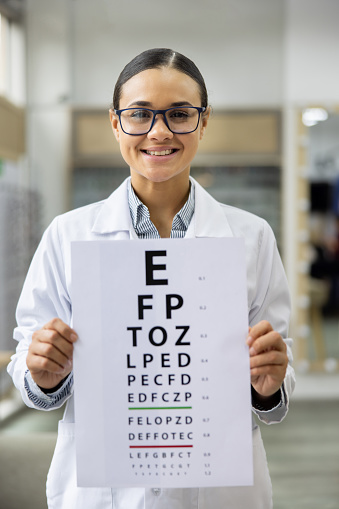 Happy Latin American optician holding a placard with letters for an eye exam