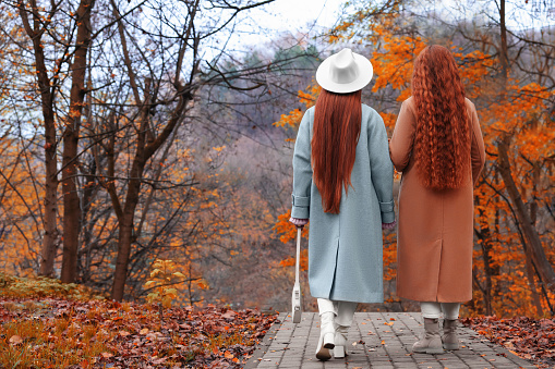 Redhead sisters walking together in park on autumn day, back view. Space for text